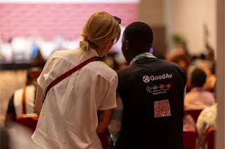 A GoodAv technician in a branded vest assisting a woman at a corporate event or conference.